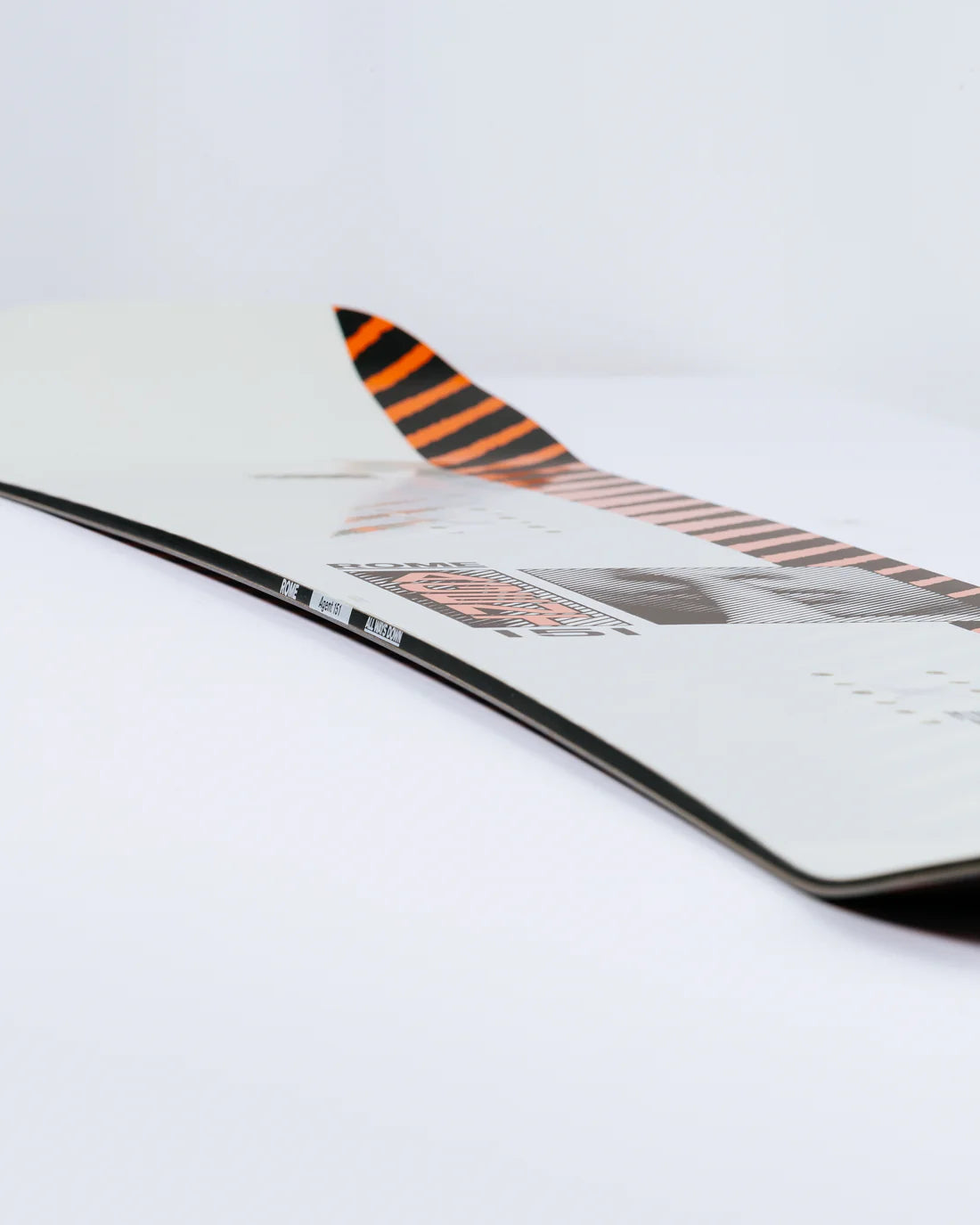 Rome Agent Snowboard 2025 - White snowboard with black and orange stripes on top of tail.