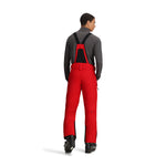 Obermeyer Force Insulated Suspender Pant 2025 - A pair of red snow pants with black suspenders and a black zipper on the left leg.