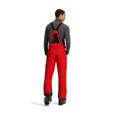Obermeyer Force Insulated Suspender Pant 2025 - A pair of red snow pants with black suspenders and a black zipper on the left leg.