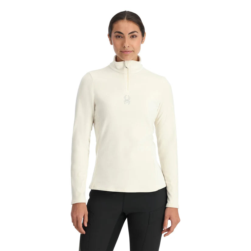 Spyder Women's Shimmer Bug 1/2 Zip Fleece 2025 - A woman wearing a white fleece top with a zipper and a small embroidered bug logo on the chest.