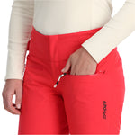Spyder Women's Winner Insulated Pants 2025 - A pair of red ski pants with a black logo on the left leg, featuring a zippered pocket and a drawstring waistband.