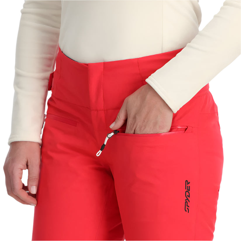 Spyder Women's Winner Insulated Pants 2025 - A pair of red ski pants with a black logo on the left leg, featuring a zippered pocket and a drawstring waistband.
