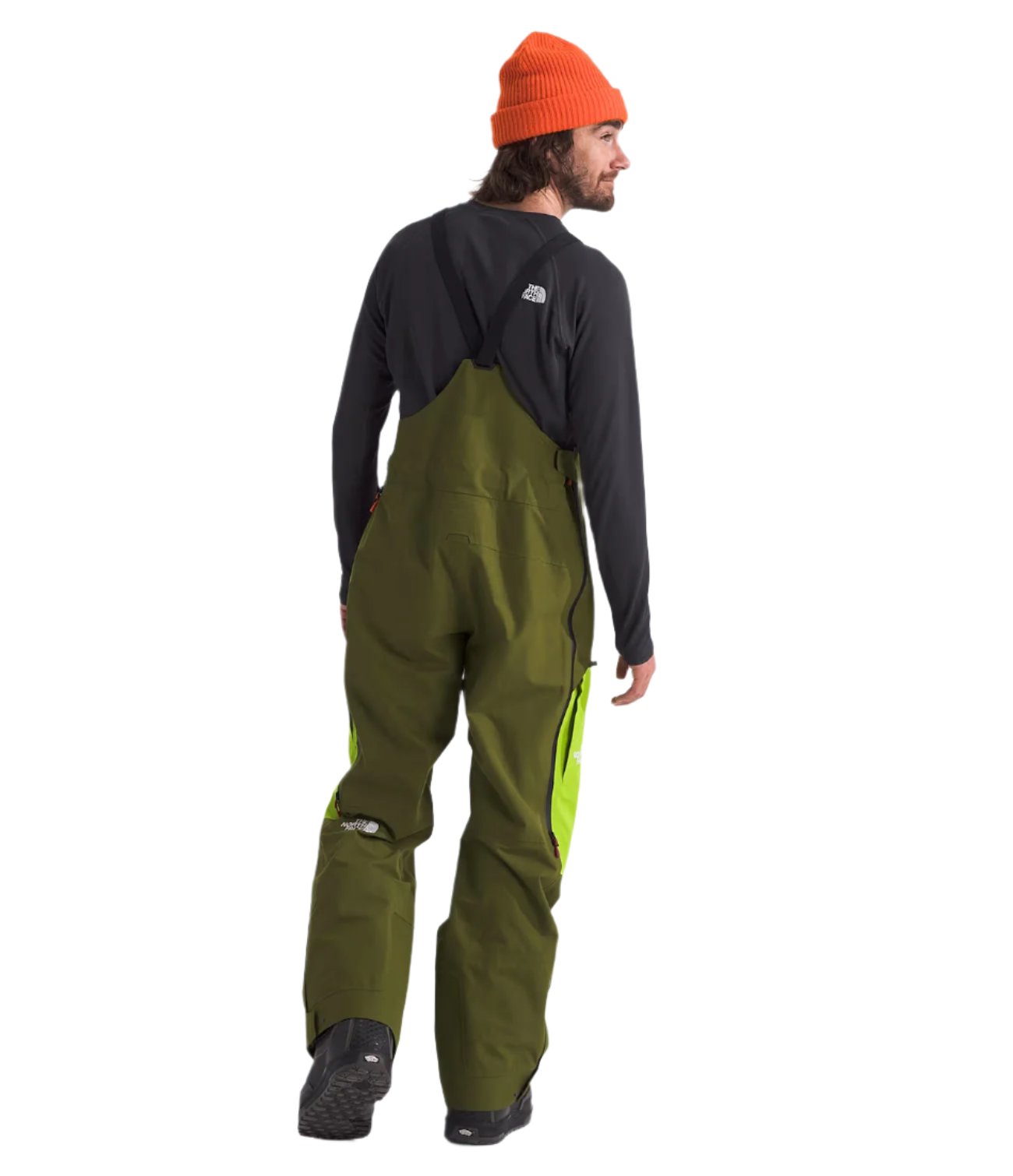North Face Men's Ceptor Shell Bib - A man wearing a pair of olive green bib overalls with neon yellow accents on the side seams and black boots.