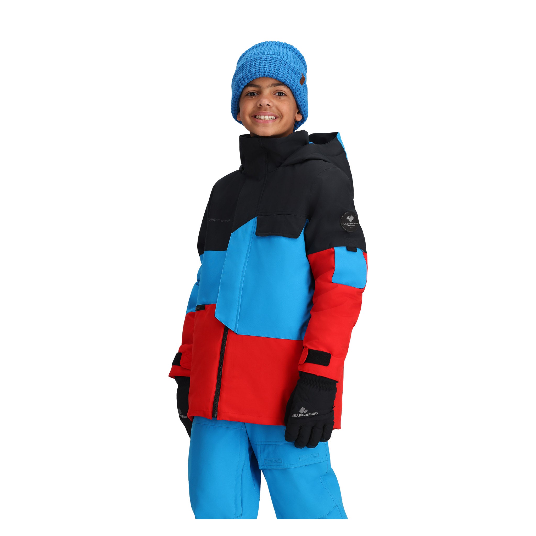 Obermeyer Junior's Axel Insulated Jacket 2025 - A black, blue and red jacket with a hood on a young boy wearing matching pants.