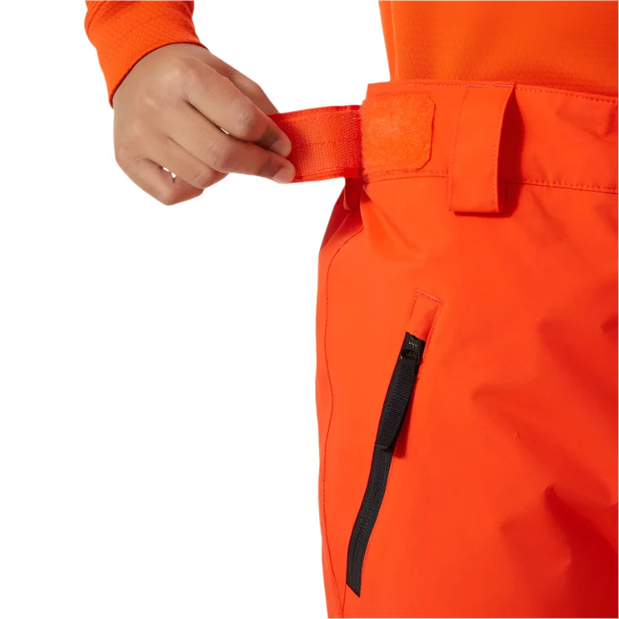 Helly Hansen Junior's Legendary Insulated Pant 2025 - A pair of bright orange insulated ski pants with a black zipper on the side pocket.