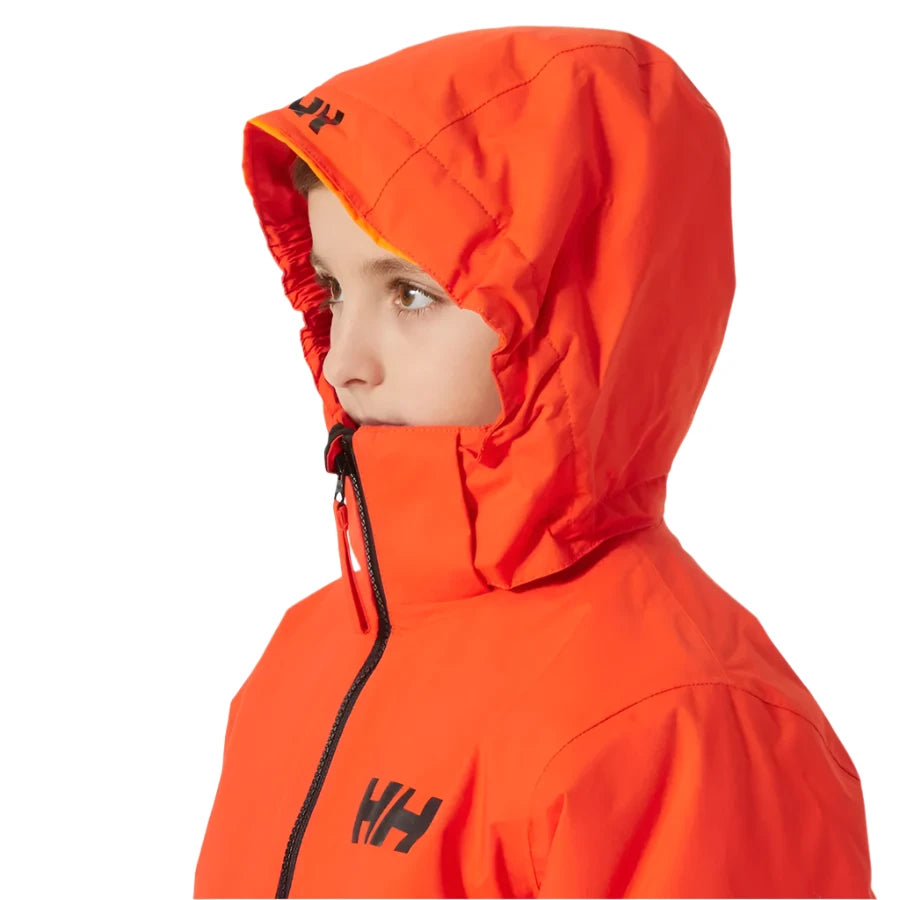 Helly Hansen Junior's Traverse Insulated Jacket - A young boy wearing a bright orange jacket with black lettering and a zipper, looking to the left side of the image.