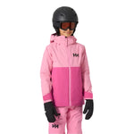 Helly Hansen Junior's Traverse Insulated Jacket 2025 - A young child wearing a pink and light-pink jacket with a hood, black gloves, and a black helmet.