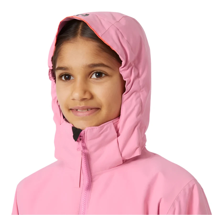 Helly Hansen Junior's Traverse Insulated Jacket 2025 - A young girl wearing a pink jacket with a hood, smiling directly at the camera.