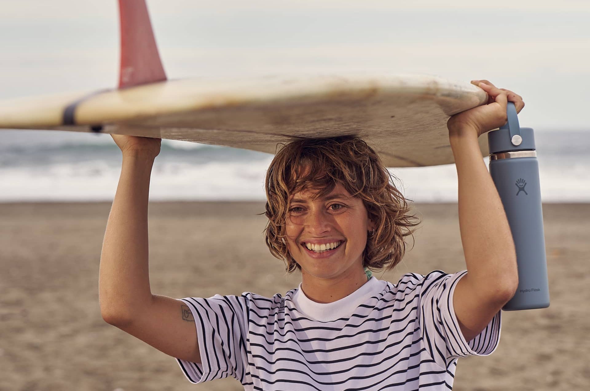 Girl holding surfboard and Hydro Flask