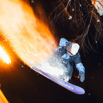 Beyond Medals Fullzip Insulated Jacket 2025 - A person in a blue and black jacket with white snowboard boots is jumping on a snowboard, wearing a white helmet and goggles.