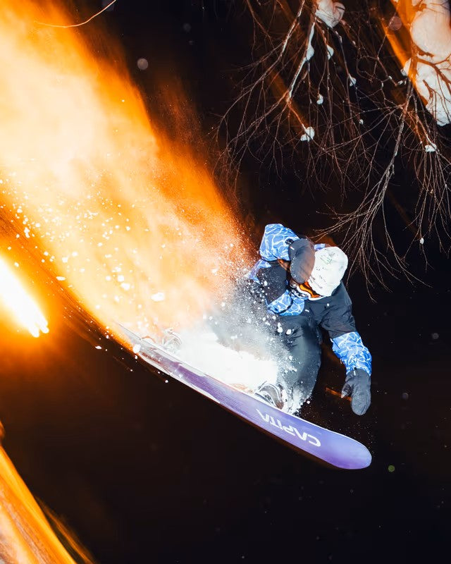 Beyond Medals Fullzip Insulated Jacket 2025 - A person in a blue and black jacket with white snowboard boots is jumping on a snowboard, wearing a white helmet and goggles.