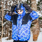 Beyond Medals Fullzip Insulated Jacket 2025 - A blue and white snowflake patterned jacket with a hood, worn by a model in front of snowy trees.