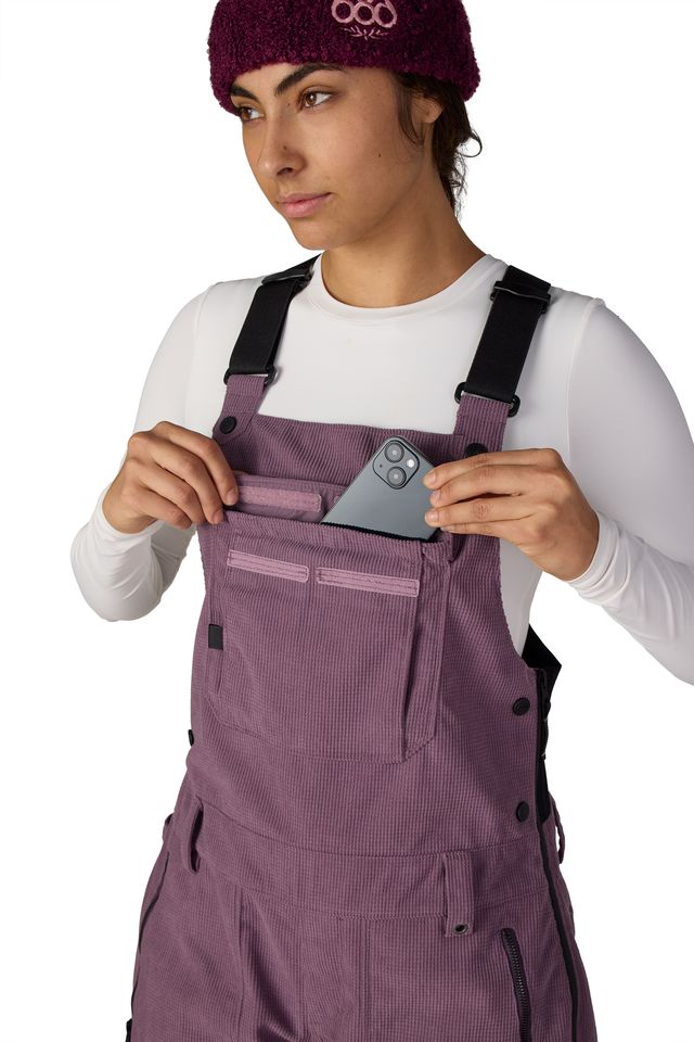 Women’s mauve purple insulated bib overalls with chest pocket, button straps, and utility details.