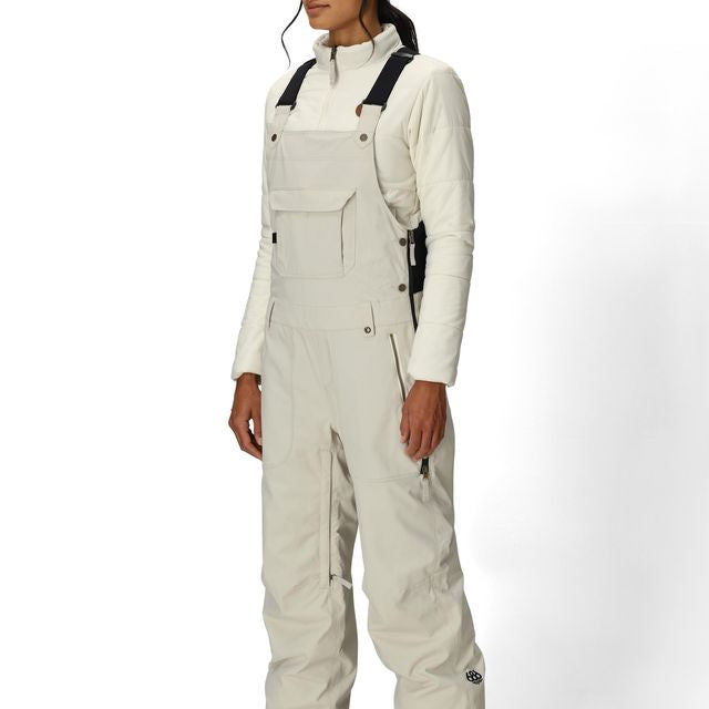 Women’s insulated bib overalls in off-white with front pockets, suspenders, and ankle cuffs.