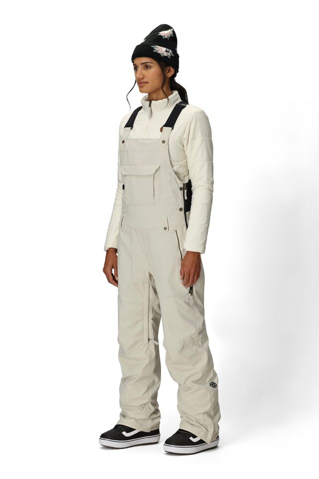 Women’s insulated bib overalls in off-white with front pockets, suspenders, and ankle cuffs.