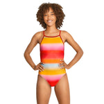 Speedo The One Printed One Piece Swimsuit - A woman with curly brown hair and a tan is wearing a one-piece swimsuit that has horizontal stripes in shades of pink, orange, yellow, blue, and red.