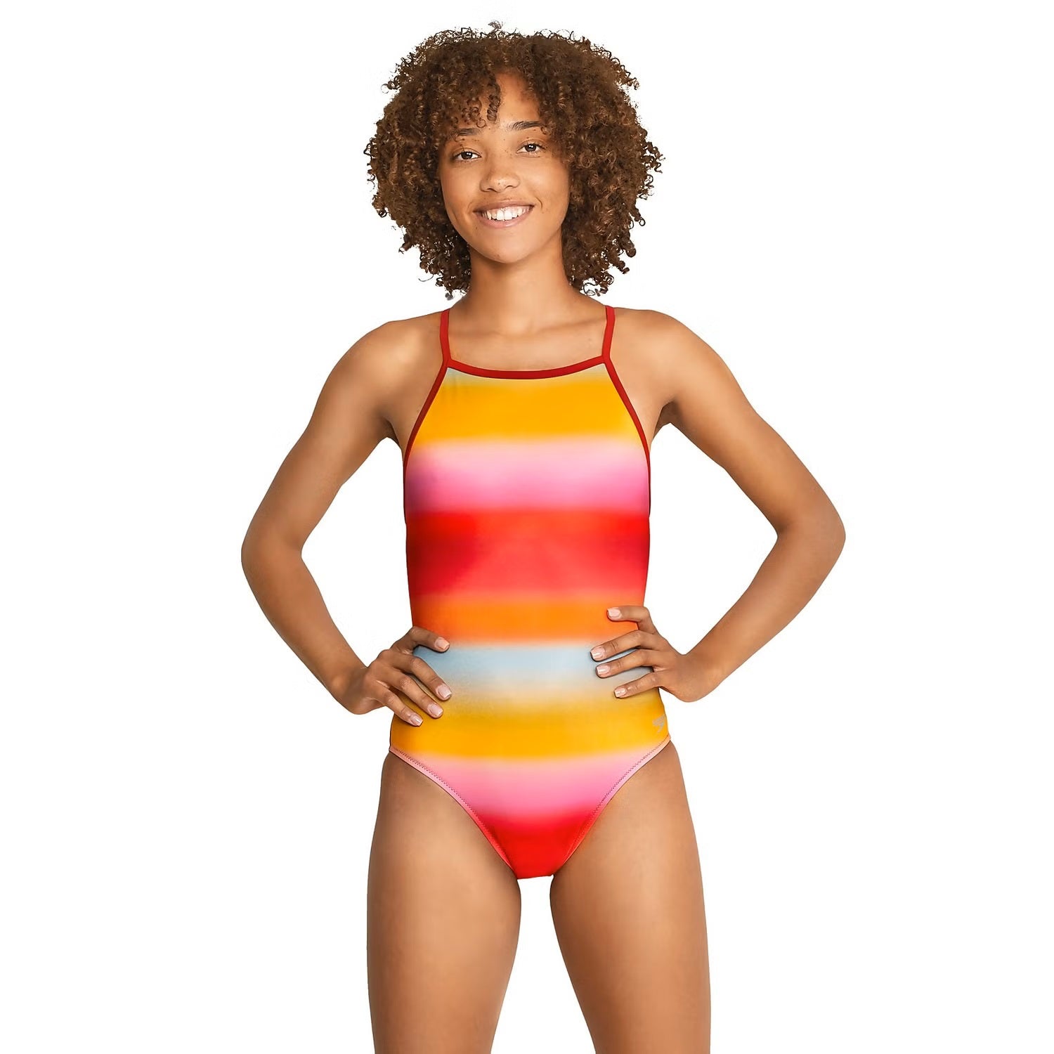 Speedo The One Printed One Piece Swimsuit - A woman with curly brown hair and a tan is wearing a one-piece swimsuit that has horizontal stripes in shades of pink, orange, yellow, blue, and red.
