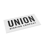 Union Surf Stomp Pad 2025 - A white surfboard pad with a repeating pattern of small, dark gray waves and a darker gray border around the edges.