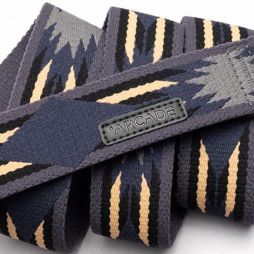 Close-up view of a dark grey belt with a geometric pattern in shades of grey and beige, showing a fabric tag with the word 'Arcade' stitched on it.