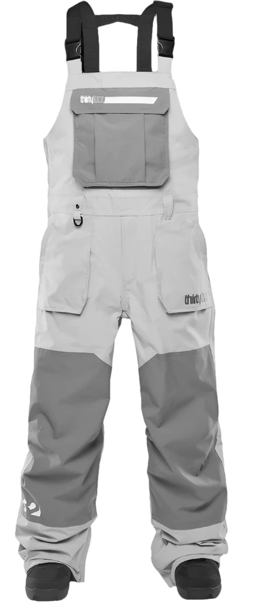ThirtyTwo Basement Shell Bib Pant 2025 - A pair of light gray snowboard pants with a reflective logo on the left thigh and a zippered pocket on the right hip.