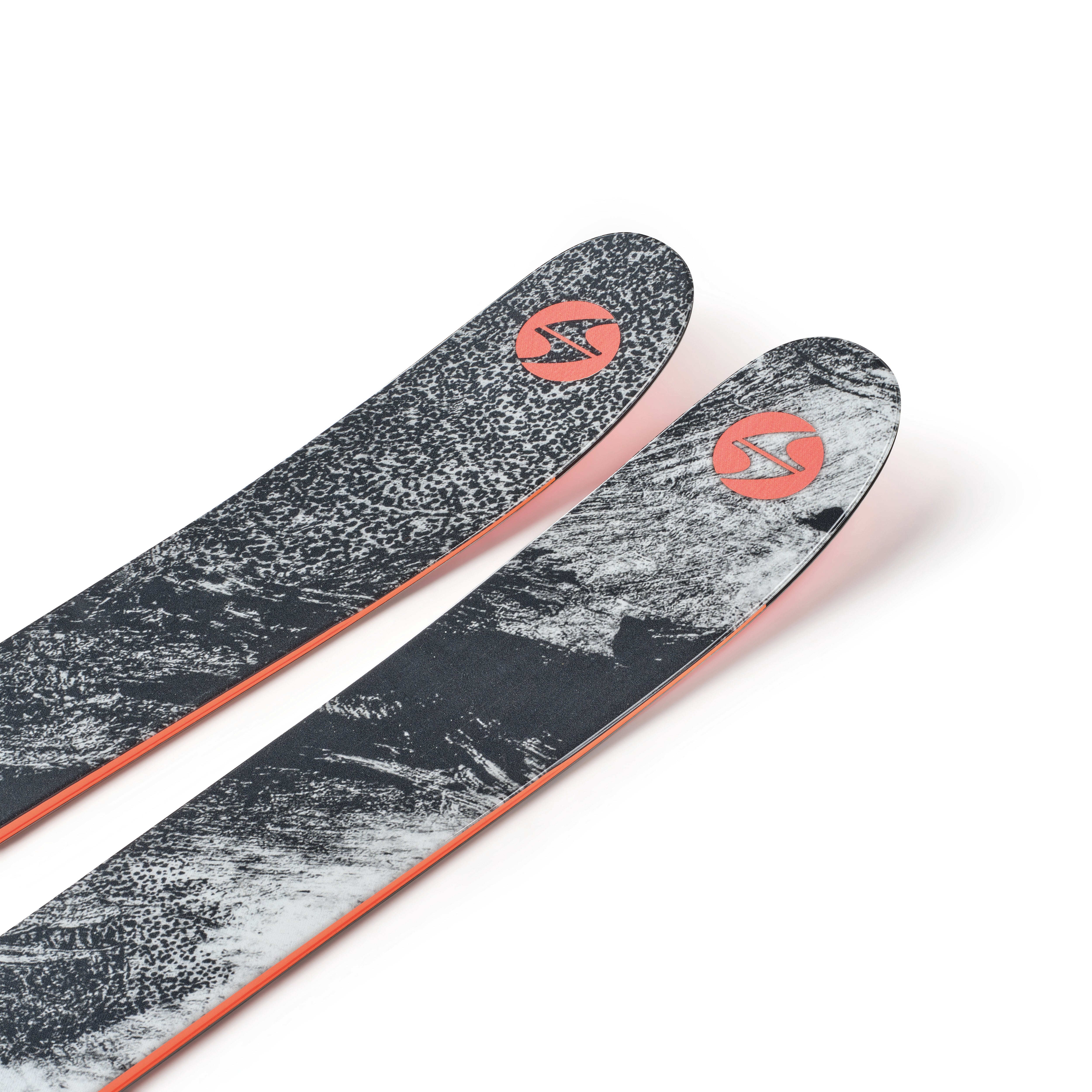 Two black skis with gray speckled tops and orange edges, angled view