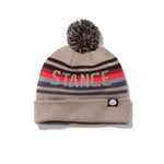 Stance OG Pom Beanie 2024 - A tan beanie with a large gray pom-pom on top and a repeating pattern of red, blue, black, and light brown stripes around the middle.