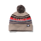 Stance OG Pom Beanie 2024 - A tan beanie with a large gray pom-pom on top and a repeating pattern of red, blue, black, and light brown stripes around the middle.