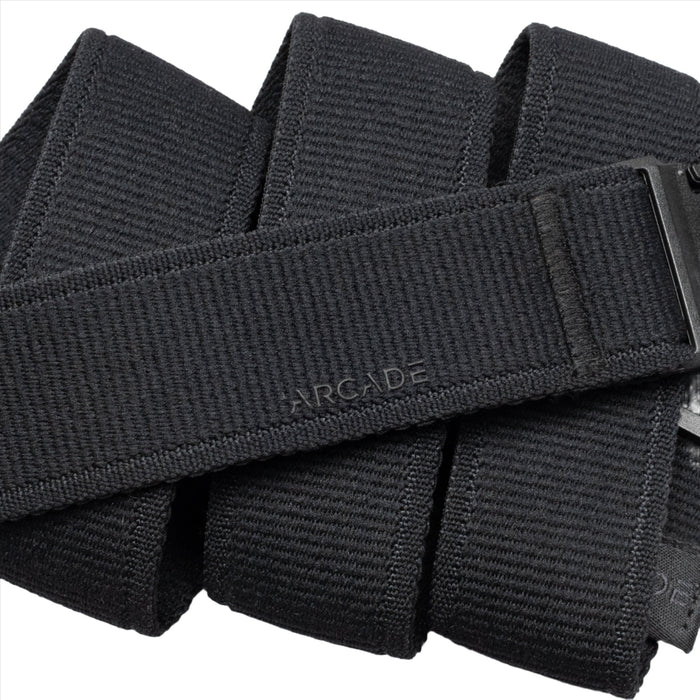 A close-up of a black fabric belt with the word 'ARCADE' embossed on the surface. The belt is folded multiple times, highlighting its texture.