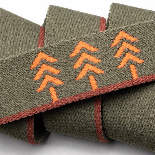 Close-up of the olive green belt showing the detailed orange embroidered chevron arrows and orange edging, along with the small leather patch.