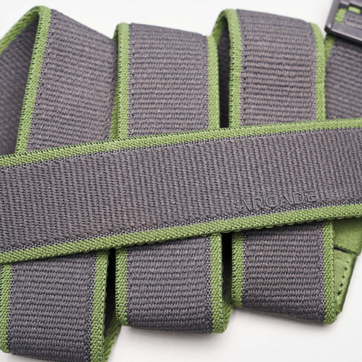 A close-up of a grey fabric belt with green edges, showing the word 'ARCADE' embossed on the surface. The belt is folded multiple times, displaying its texture and stitching details.