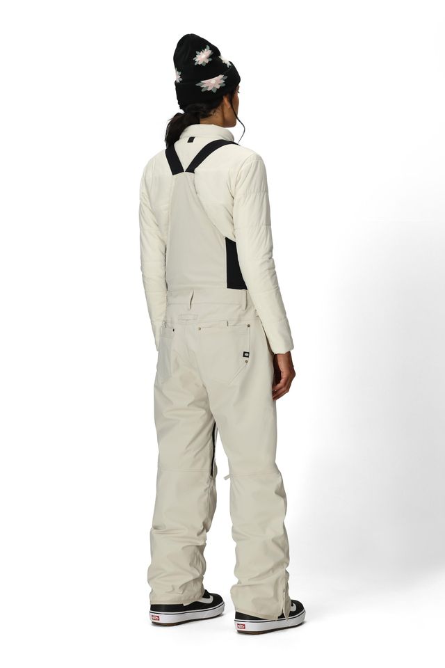 Women’s insulated off-white bib overalls, back view with full suspenders and pocket details.