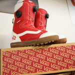 Vans Women's Encore Pro Limited Edition Snowboard Boots 2026 - A pair of red and white snowboard boots with black buckles, sitting atop a cardboard box.