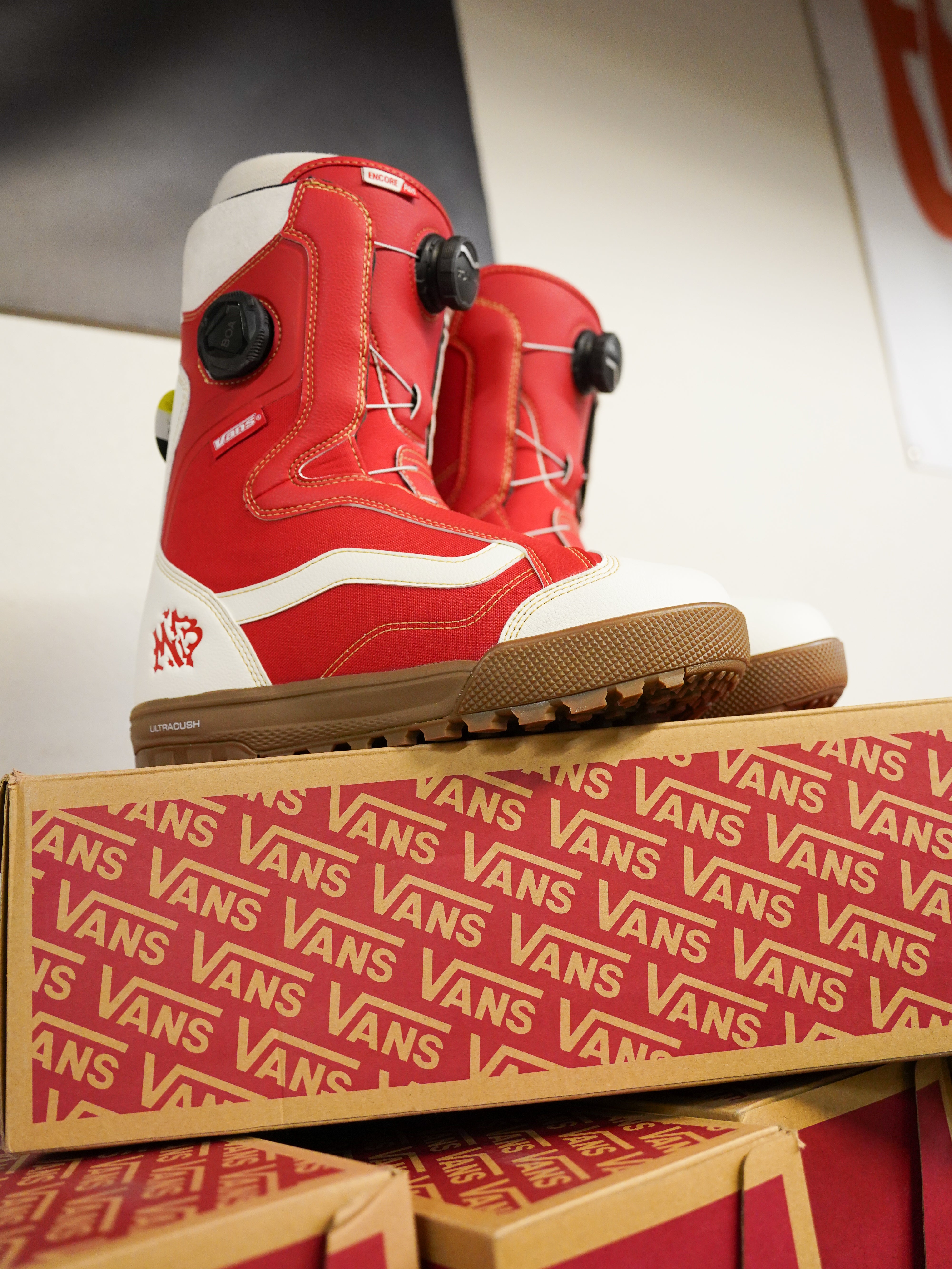 Vans Women's Encore Pro Limited Edition Snowboard Boots 2026 - A pair of red and white snowboard boots with black buckles, sitting atop a cardboard box.