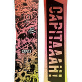 CAPiTA - Junior's Scott Stevens Mini Snowboard 2025 is a snowboard with a pink background and black graphics of various cartoon characters, including a smiling face, a fish, and a dog.