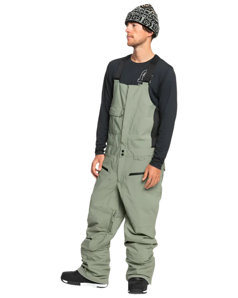 Quiksilver Utility Shell Bib - A pair of olive green snow pants with a zippered pocket on the thigh and adjustable Velcro straps at the waist.