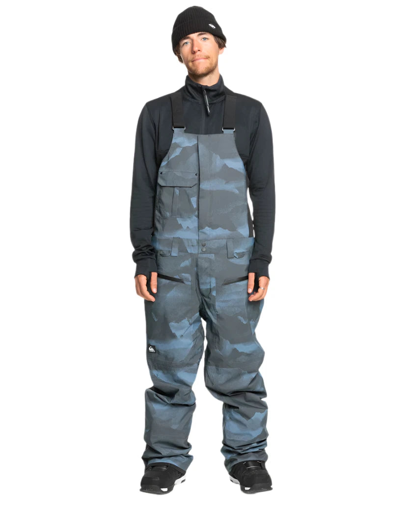 Quiksilver Utility Shell Bib - A pair of dark gray snow pants with a subtle black pattern and two zippered pockets on the side.