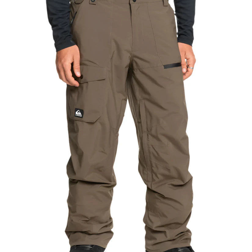 Quiksilver Utility Shell Pant 2025 - A pair of khaki-colored snow pants with a black logo patch on the left thigh and two zippered pockets on the right leg.