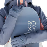 Roxy Women's Freshfield Glove 2025 - A woman wearing a gray snowboard jacket with pink accents holds a light blue snowboard in front of her torso, showcasing the glove on her left hand.