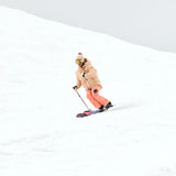 Roxy Women's Alofted Puffy Insulated Jacket - A woman in a tan puffer jacket with brown fur trim, wearing goggles and snow pants, skiing down a snowy hill.