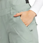 Roxy Women's Rideout Insulated Bib Pant 2025 - A pair of light gray snow pants with a black stripe down the side, featuring a zippered pocket on the thigh and a snap button closure at the waist.