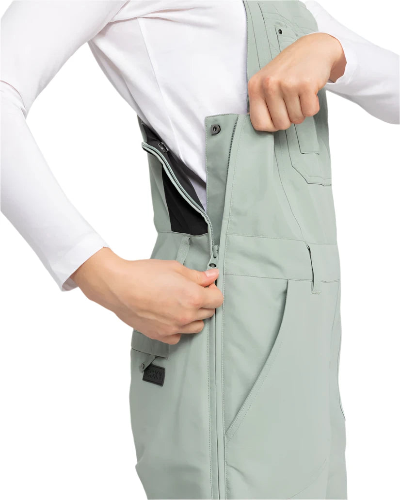 Roxy Women's Rideout Insulated Bib Pant 2025 - A pair of light gray snow pants with a black waistband and two zippered pockets on the front.