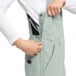 Roxy Women's Rideout Insulated Bib Pant 2025 - A pair of light gray snow pants with a black waistband and two zippered pockets on the front.