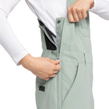 Roxy Women's Rideout Insulated Bib Pant 2025 - A pair of light gray snow pants with a black waistband and two zippered pockets on the front.