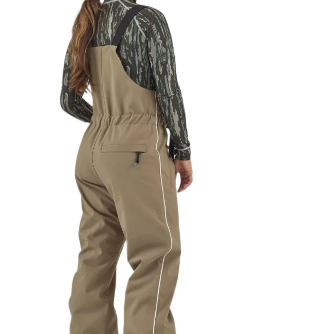 Airblaster Women's Every Body Insulated Bib - A woman wearing a black and white camouflage patterned long-sleeved shirt, khaki bib overalls with white piping down the side seam, and gray snow boots.