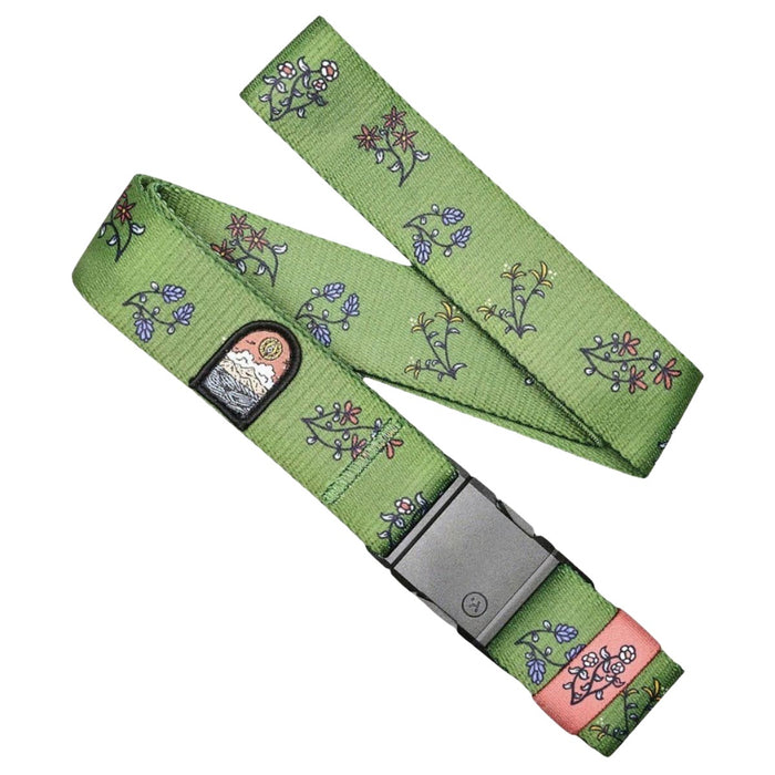 A green belt with a pattern of small flowers in various colors, including pink, blue, and white. The belt has a metal buckle and a small patch with an embroidered design of a sunset over mountains.