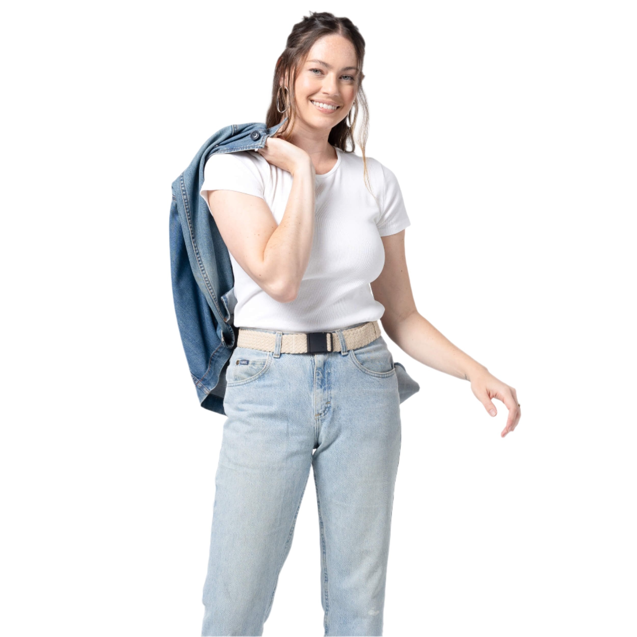 Arcade Futureweave Belt 2025 - A woman with long brown hair, wearing a white t-shirt and light-washed jeans, holds up a blue denim jacket over her right shoulder. The belt is beige with a black buckle.