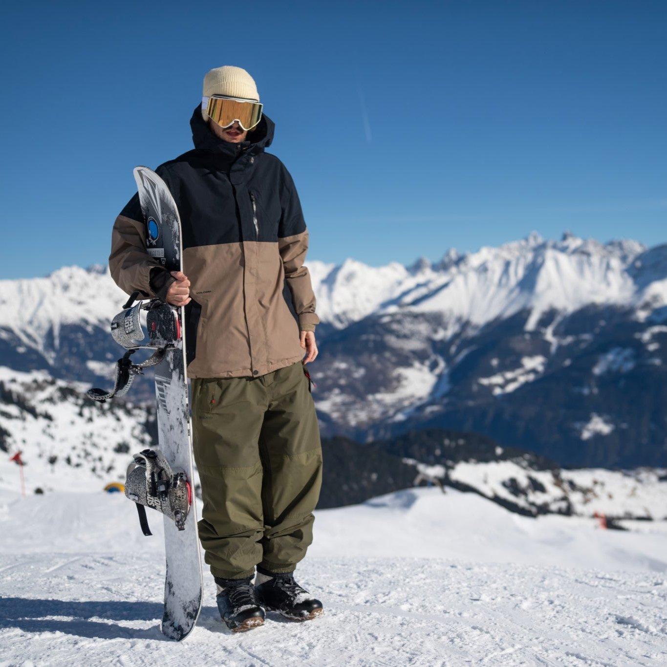 Volcom 2L Insulated GORE-TEX Jacket - A black and brown jacket with a hood, worn by a model on a snowy mountain top.