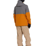 Volcom Men's Rain GORE-TEX Bib Overall - A man wearing a grey and orange rain jacket, khaki bib overalls with cargo pockets, black gloves, and black sneakers.