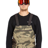 Volcom Men's Roan Shell Bib Overall - A pair of khaki-colored bib overalls with a camouflage pattern, featuring two front pockets and adjustable straps.