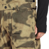 Volcom Men's Roan Shell Bib Overall - A camouflage-patterned overall with a black belt and two front pockets.